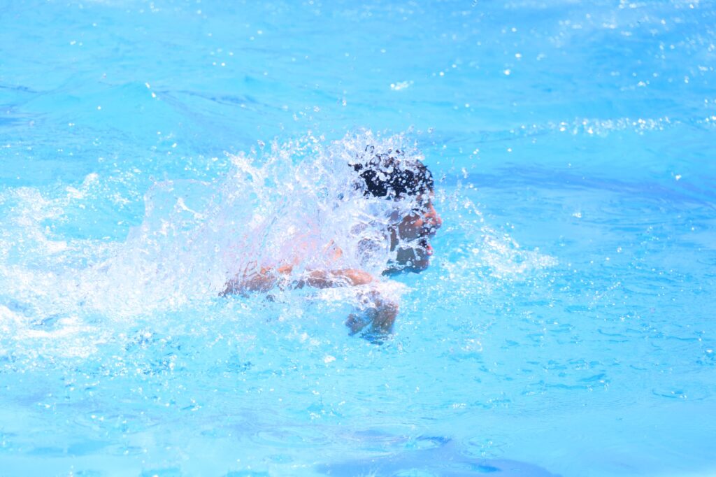 Person splashing water in a bright blue swimming pool.