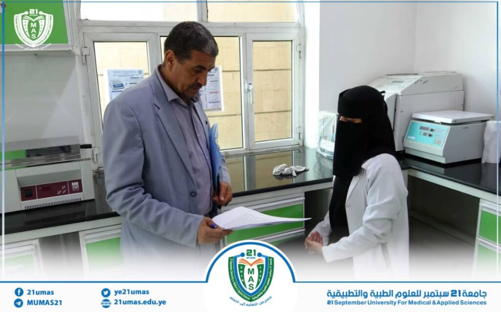 Man in a gray blazer hands documents to a woman in a black veil in a university laboratory.