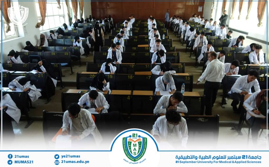 Large exam hall with students seated at numbered desks taking a test, in white shirts/uniforms.