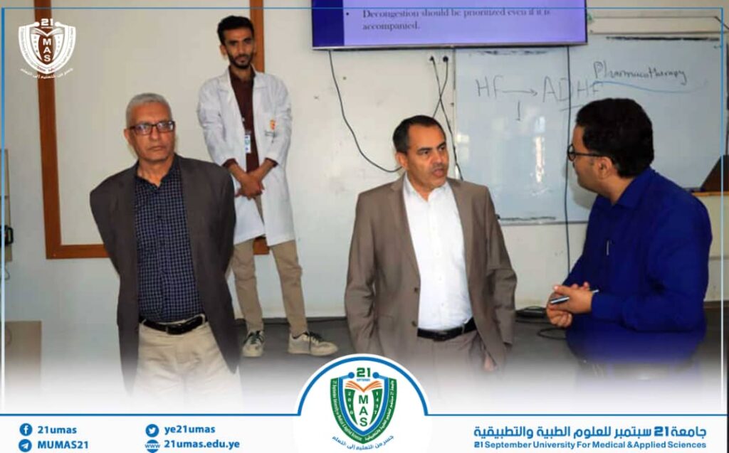 Group of four men in a classroom discussing, one in a white lab coat, with a whiteboard showing chemical notes behind them.