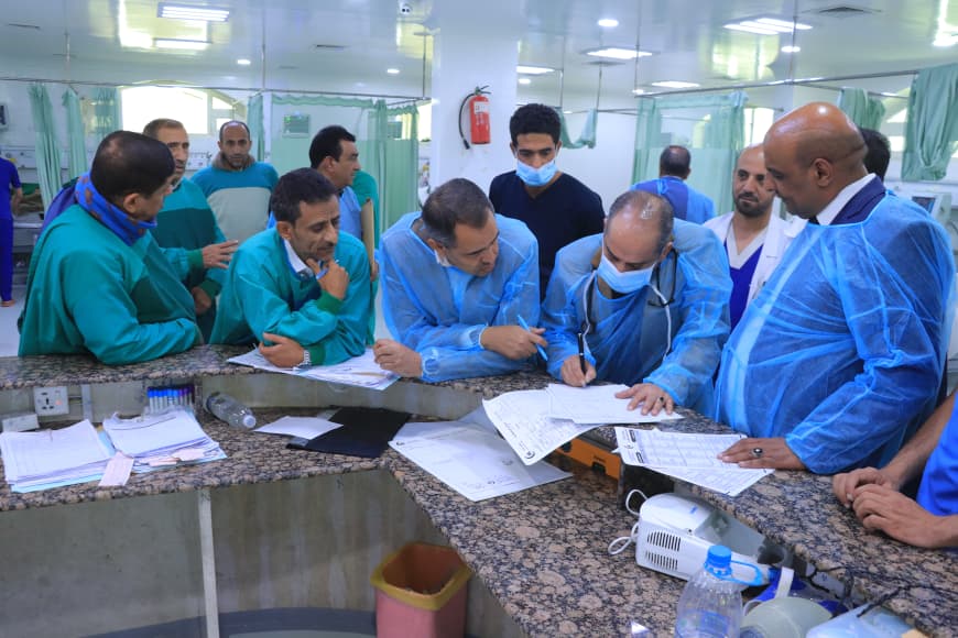 Medical team gathers around a hospital counter, reviewing and signing patient documents in scrubs and masks.