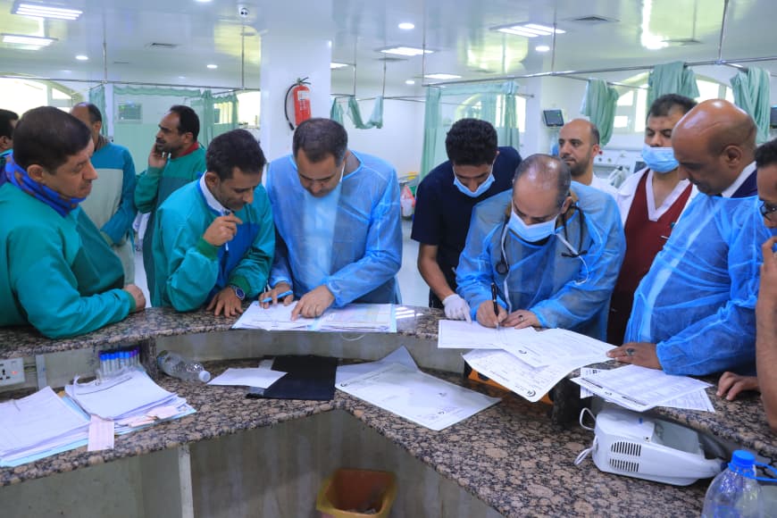 Medical team in scrubs gathered around a hospital counter, reviewing charts and signing documents.