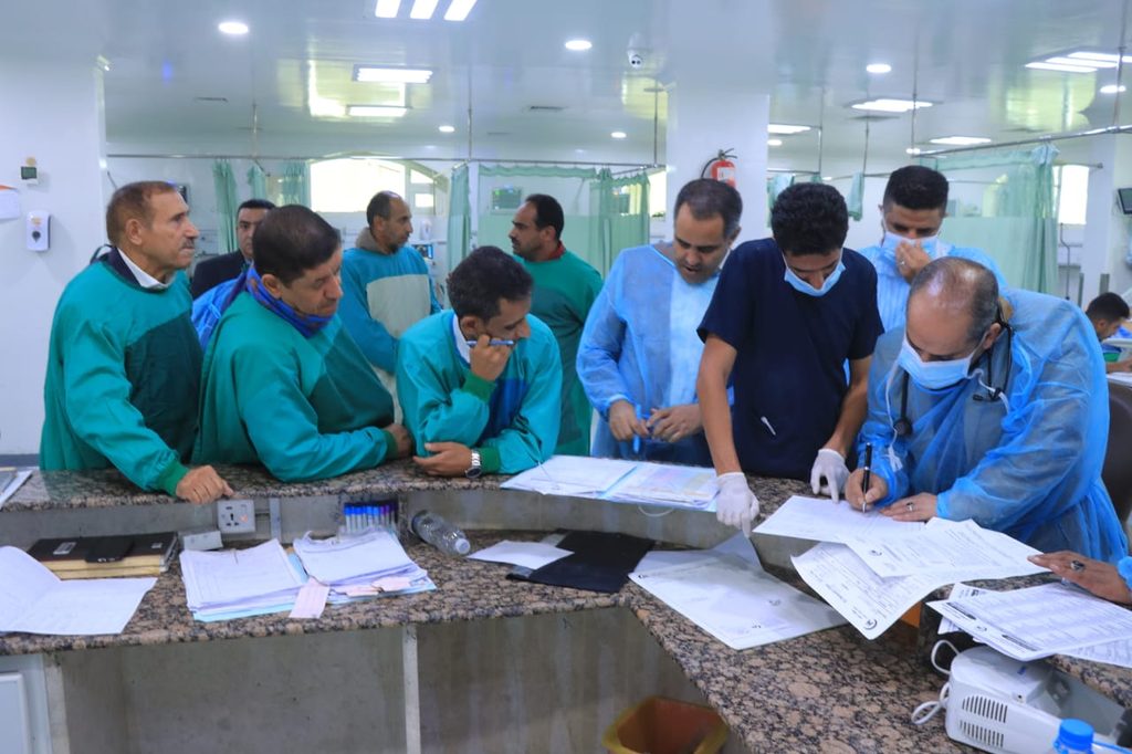 Medical staff in scrubs and masks gathered at a counter, reviewing charts and signing forms.