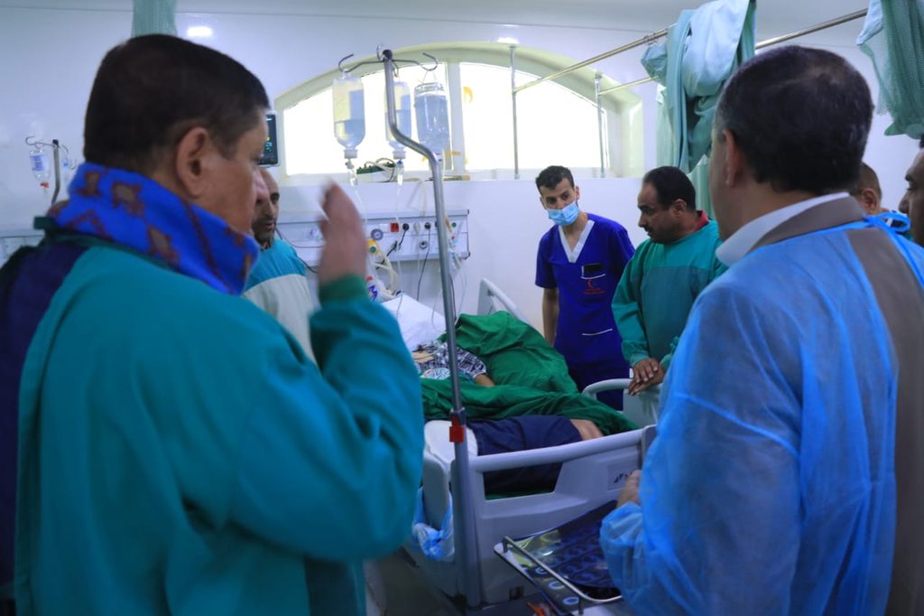 Medical team gathers around a patient lying in a hospital bed connected to IV fluids.