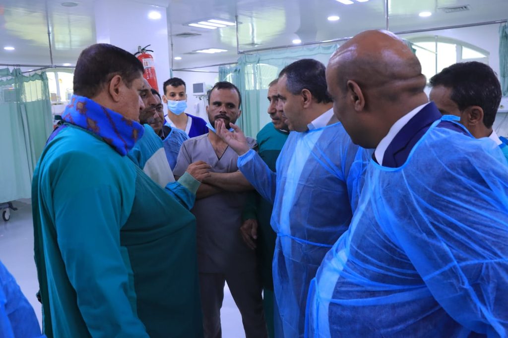 Medical team in PPE gowns having a discussion in a hospital ward with curtains drawn around patient bays.