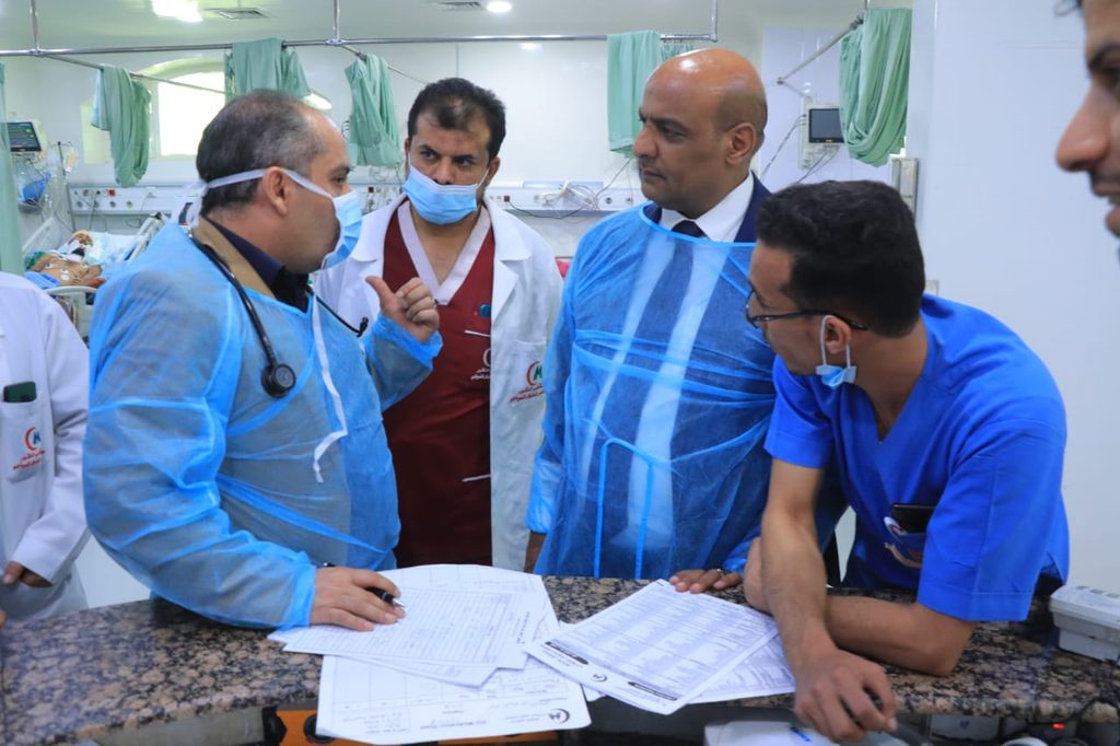Medical team in PPE reviews patient forms at a hospital desk, discussing care notes in the foreground.