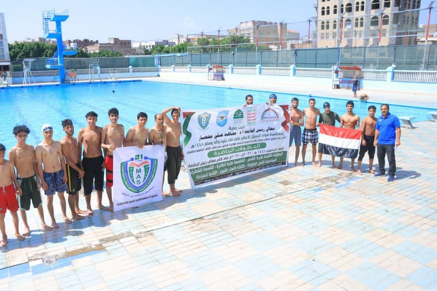 Group of young swimmers standing by a pool, holding banners and an Egyptian flag for a team event.