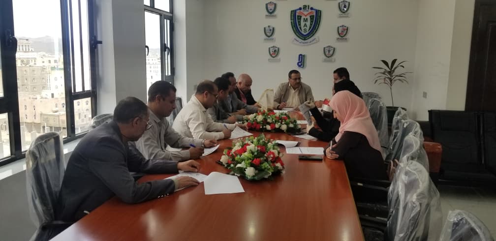 Group of professionals seated around a long conference table discussing documents in a bright office with a flower centerpiece.",