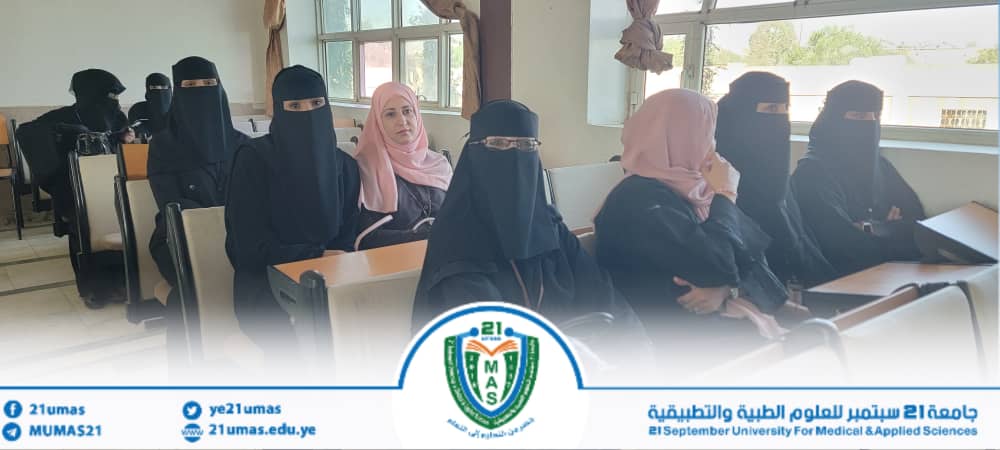 Group of veiled female students seated in a university classroom, with a blue-and-white banner at the front.