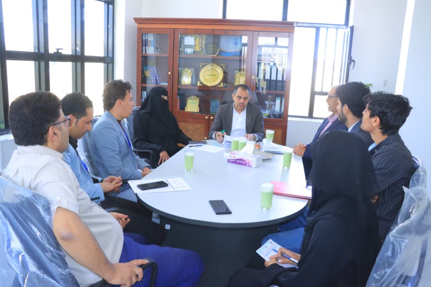 Group of professionals seated around a round table in a meeting room, discussing with papers and drinks on the table.