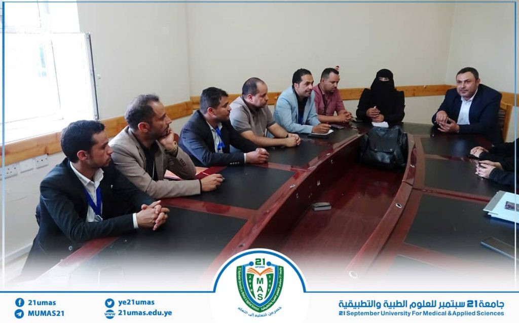 Group of professionals seated around a curved conference table in a meeting room, discussing a agenda with a logo banner at the bottom edge.