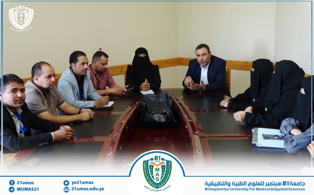 Diverse group seated around a conference table in a meeting room, discussing; university logos and a blue-bordered banner appear at the bottom.