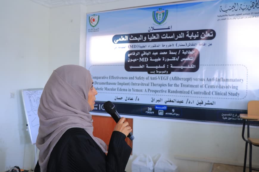 Woman wearing a hijab speaks into a microphone next to a large banner with logos and Arabic text, likely presenting at a conference.
