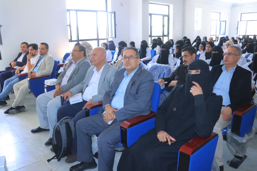 Diverse audience seated in a conference hall; front row includes men in suits and a woman in a black hijab, attentively watching a presentation at the event.