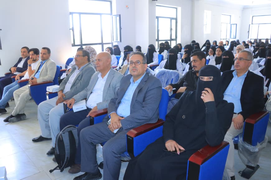 Audience seated in a conference hall; front row includes men in suits and a woman in a black niqab, with more attendees in the background.