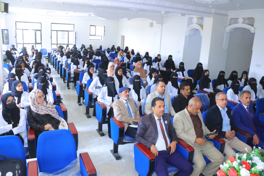 Large lecture hall filled with attendees; many women wear black niqabs, men in suits sit at the front, with a flower arrangement visible at the front.