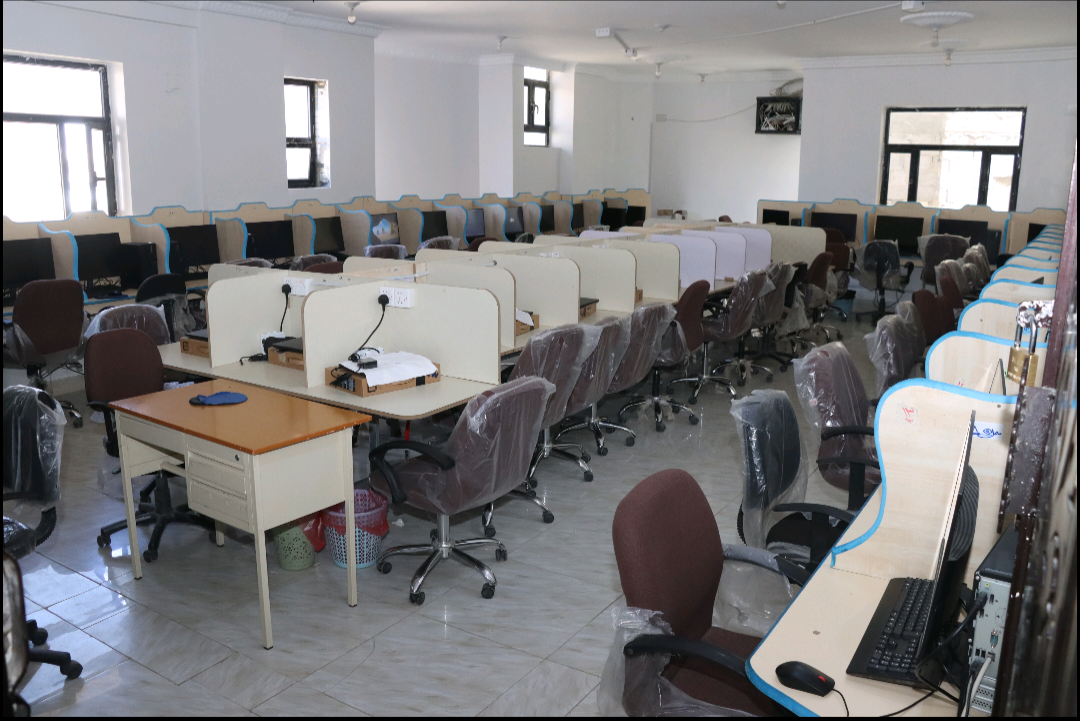 A large computer lab with rows of desks and cubicle partitions, each station equipped with a monitor and chair.